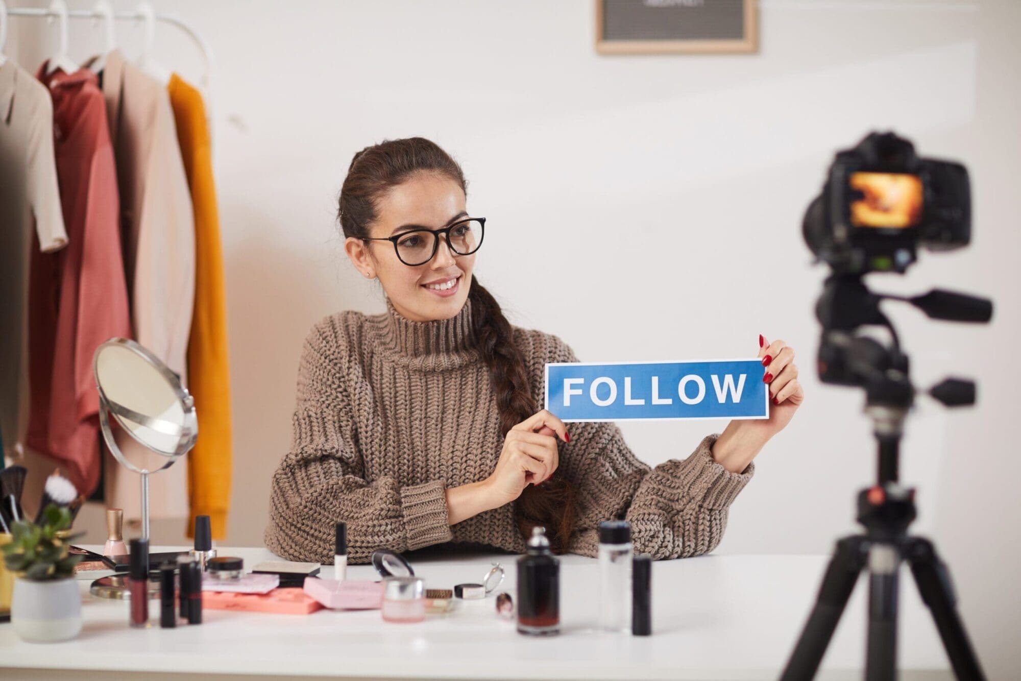 Portrait of contemporary young woman holding FOLLOW word while filming video for beauty and lifestyle channel, copy space