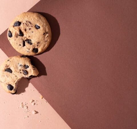 Two chocolate chip cookies on brown paper background in sunlight