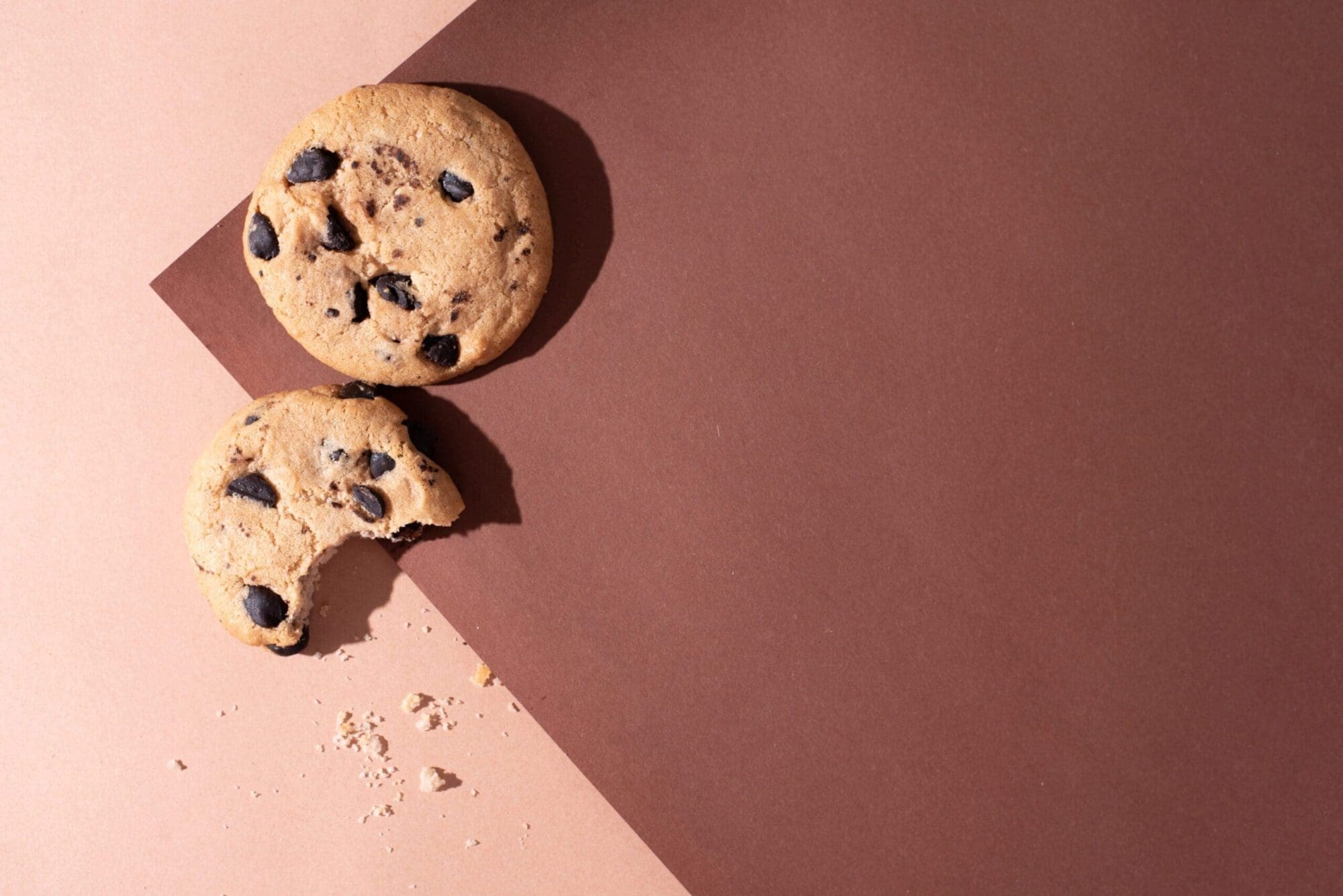 Two chocolate chip cookies on brown paper background in sunlight