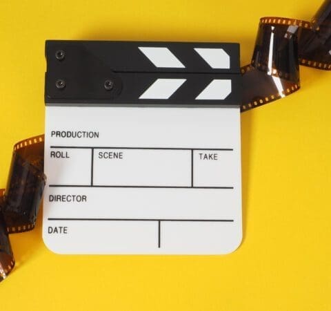 Small white clapper board and film roll on yellow background