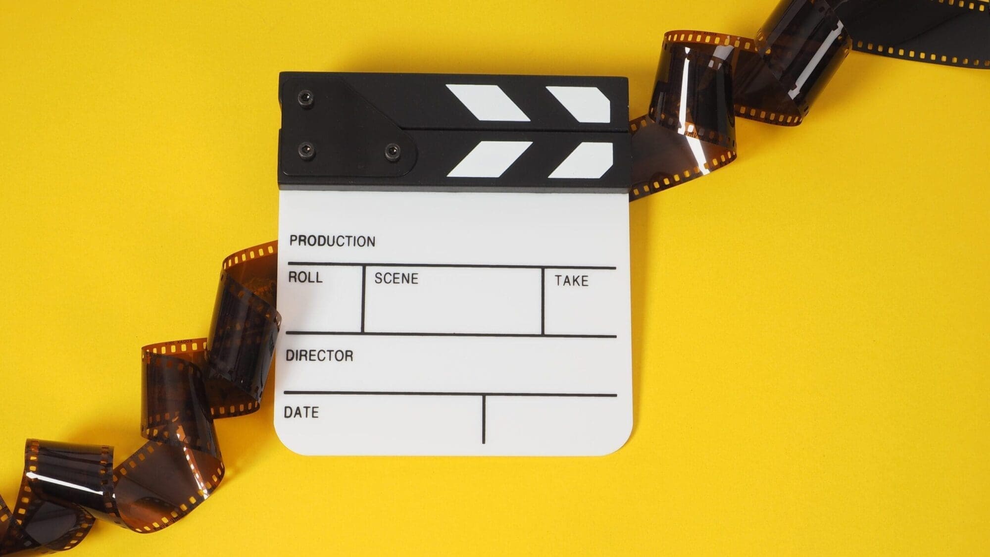 Small white clapper board and film roll on yellow background